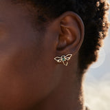 Gold dragonfly shaped earring hand-painted in green enamel and blue sapphires as eyes on model