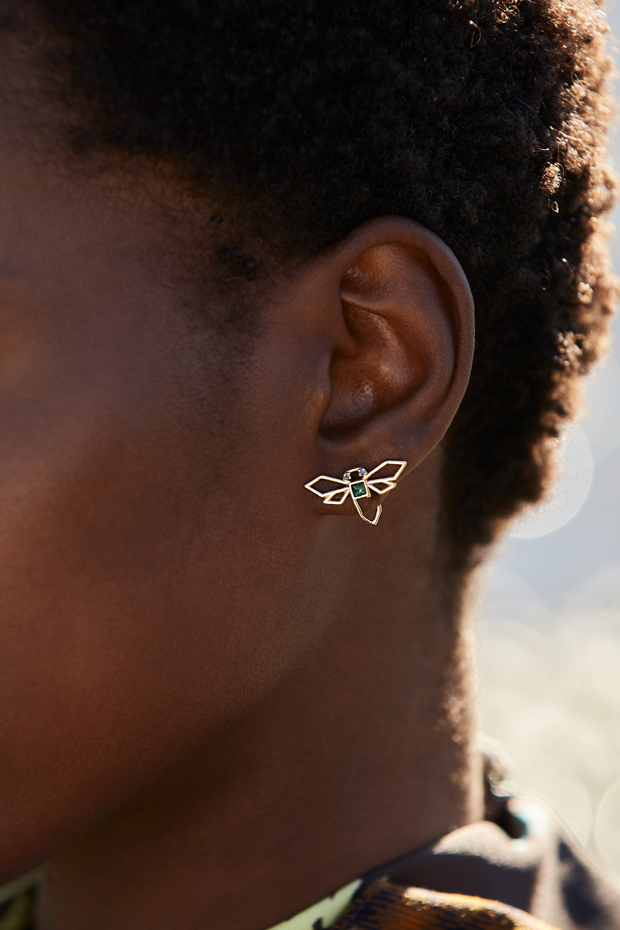 Gold dragonfly shaped earring hand-painted in green enamel and blue sapphires as eyes on model