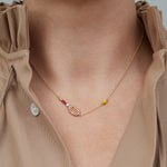 Gold chain necklace with gold tennis racquet and ball shaped pendants in pink and yellow enamel worn by model