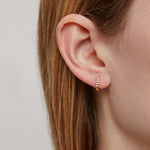 Woman wearing a gold small hoop earring with a zig-zag texture