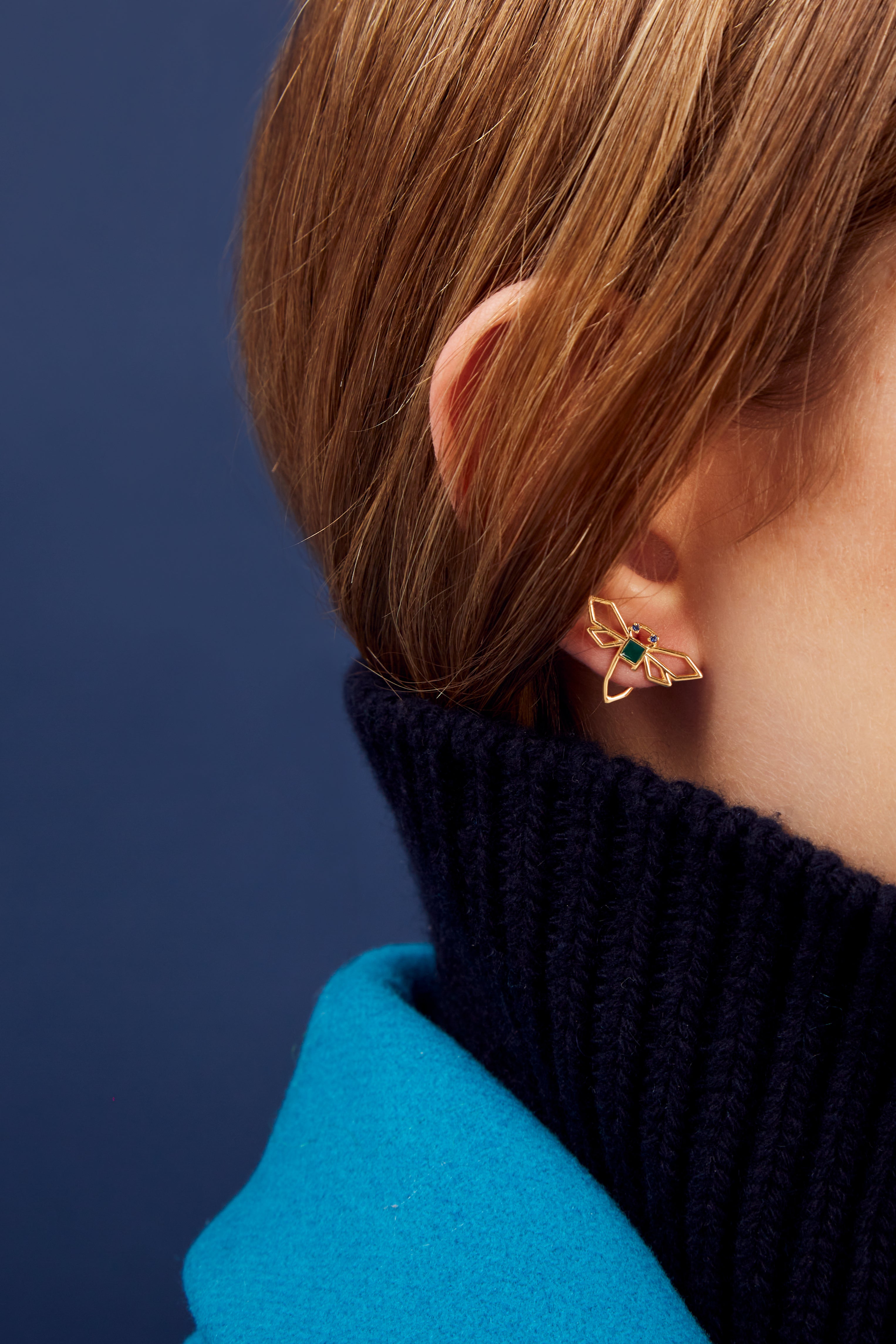 Woman wearing a dragonfly shaped gold earring with blue sapphire and green enamel