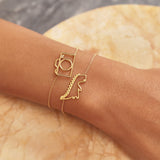 Gold chain bracelets with dinosaur and camera shaped pendant with small diamond worn by model