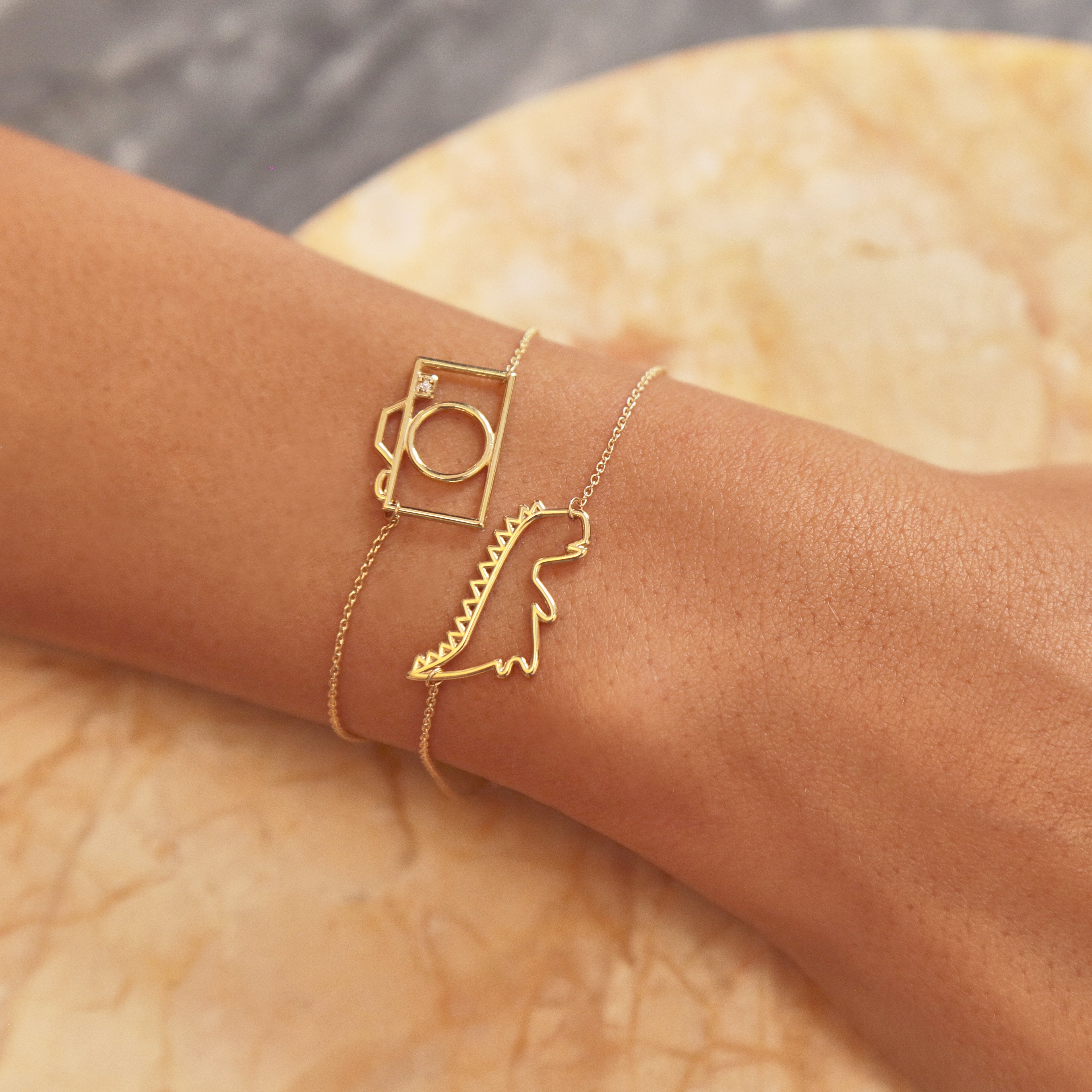 Gold chain bracelets with dinosaur and camera shaped pendant with small diamond worn by model