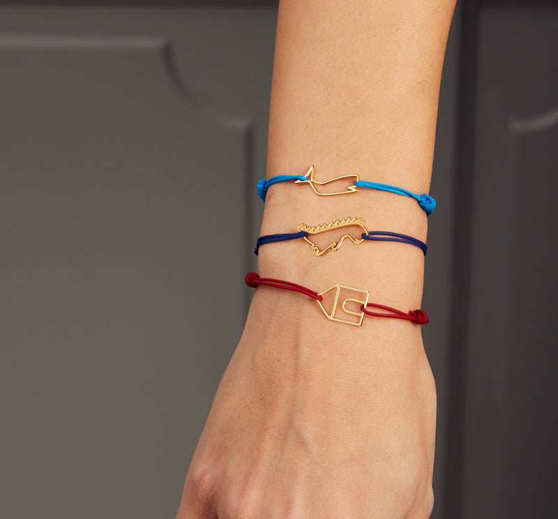Colored cord bracelets with gold pendants shaped like a whale, a dinosaur and a house on woman's arm