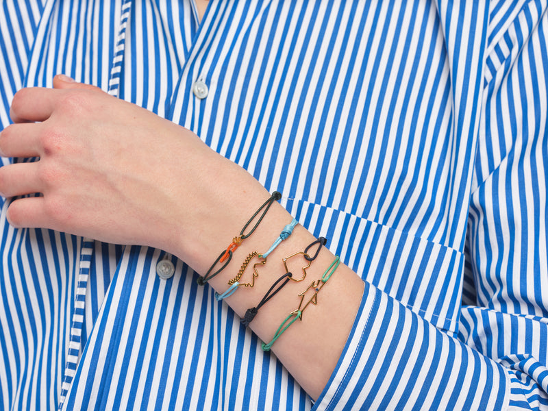 Model wearing cord bracelets with gold pendants