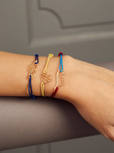 Hand wearing gold cord bracelets with gold pendants shaped like crocodile and dinosaur with stones