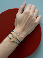 Load image into Gallery viewer, Hand wearing cord bracelets with gold robot and dinosaur shaped pendants
