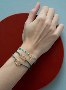 Hand wearing cord bracelets with gold robot and dinosaur shaped pendants