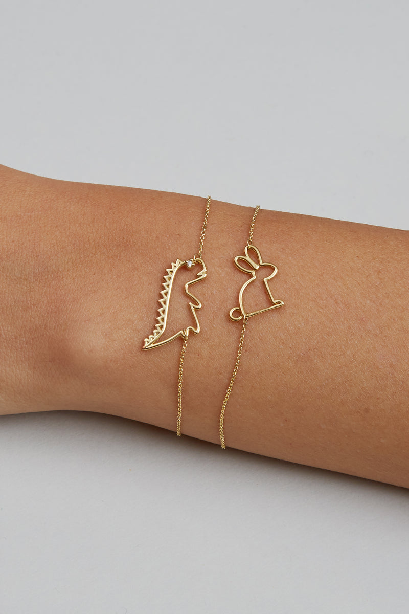 Gold chain bracelets with dinosaur and rabbit shaped pendants and small diamond worn by model