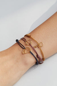 Cord bracelets with drum, igloo, ukulele gold pendants on model's wrist