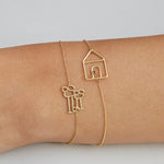 Gold chain bracelets with family and house shaped gold pendants on model's wrist
