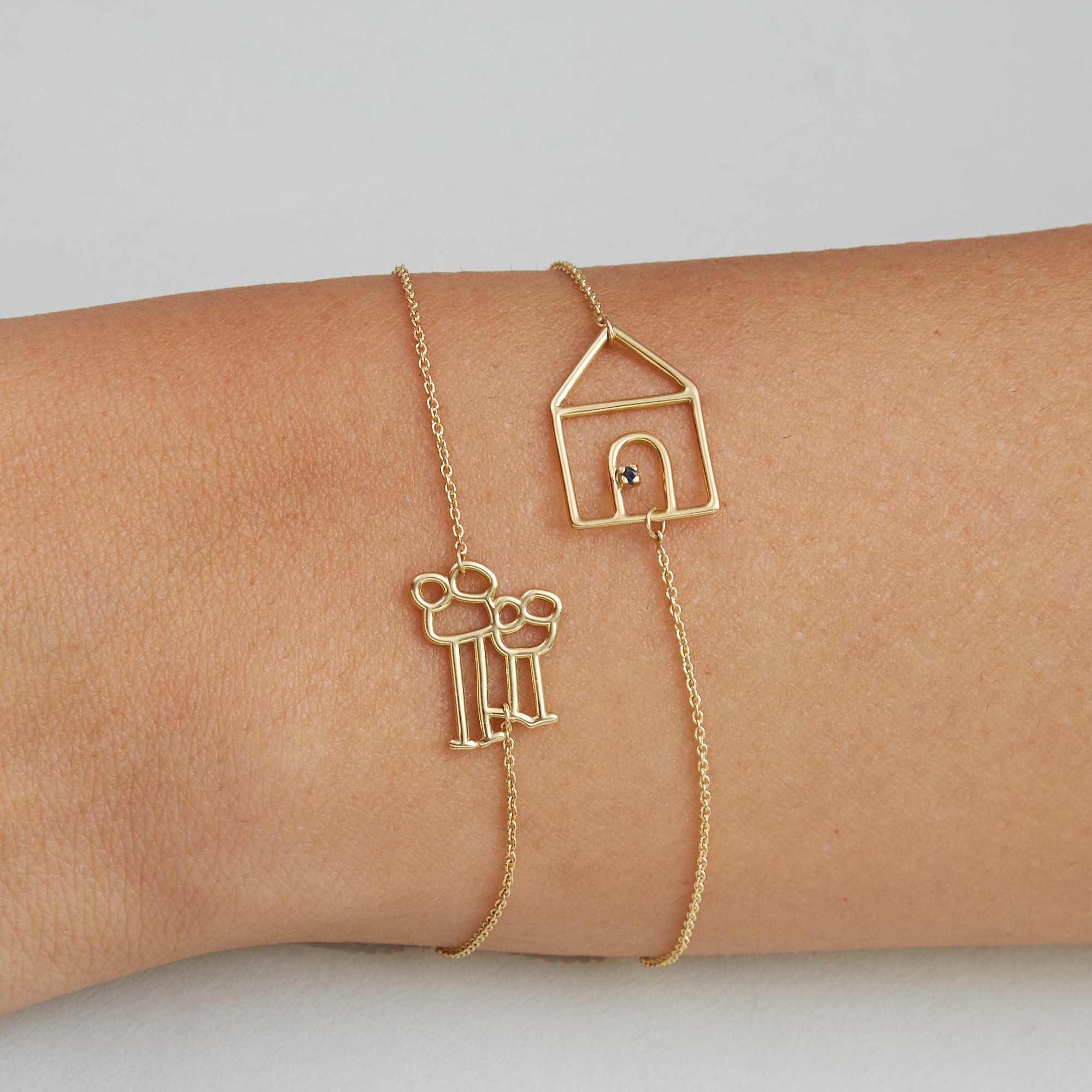 Gold chain bracelets with family and house shaped gold pendants on model's wrist