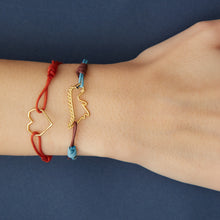 Carica l&#39;immagine nel visualizzatore di Gallery, Sky blue and burgundy cord bracelet with gold dinosaur shaped pendant and small blue sapphire worn by model
