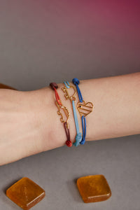 Hand with cord bracelets with gold pendants shaped like crocodile, turtle and heart with sapphire