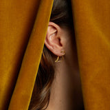 Gold dinosaur shaped earring worn by model under curtains