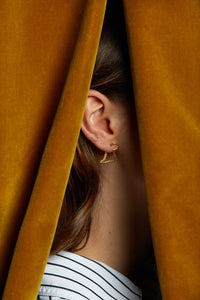 Gold dinosaur shaped earring worn by model under curtains