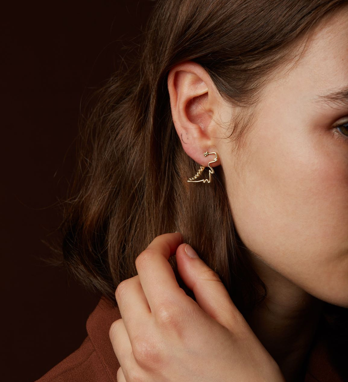 Gold dinosaur shaped earring worn by model