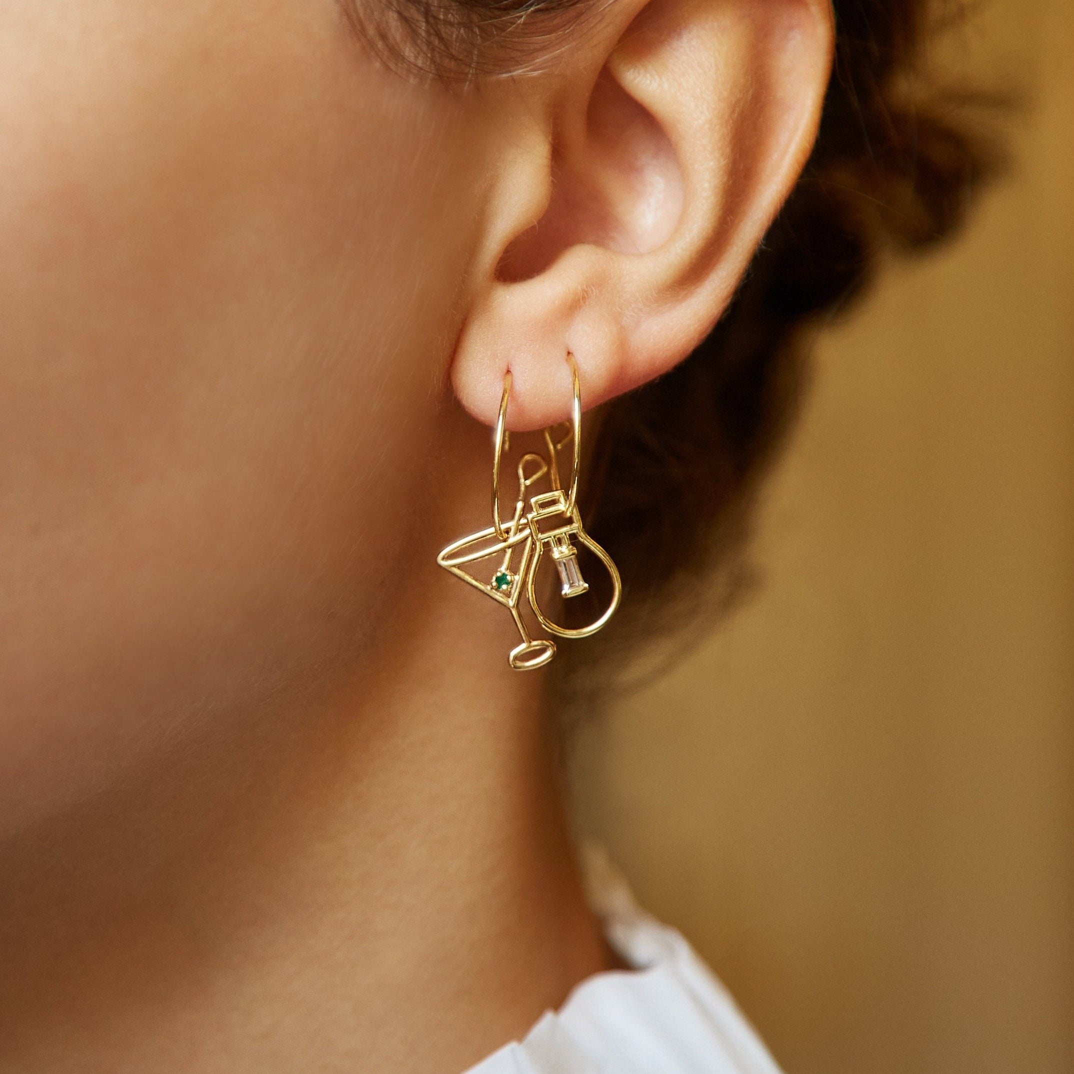 Gold hoop earring with martini drink shaped pendant and small emerald worn by model