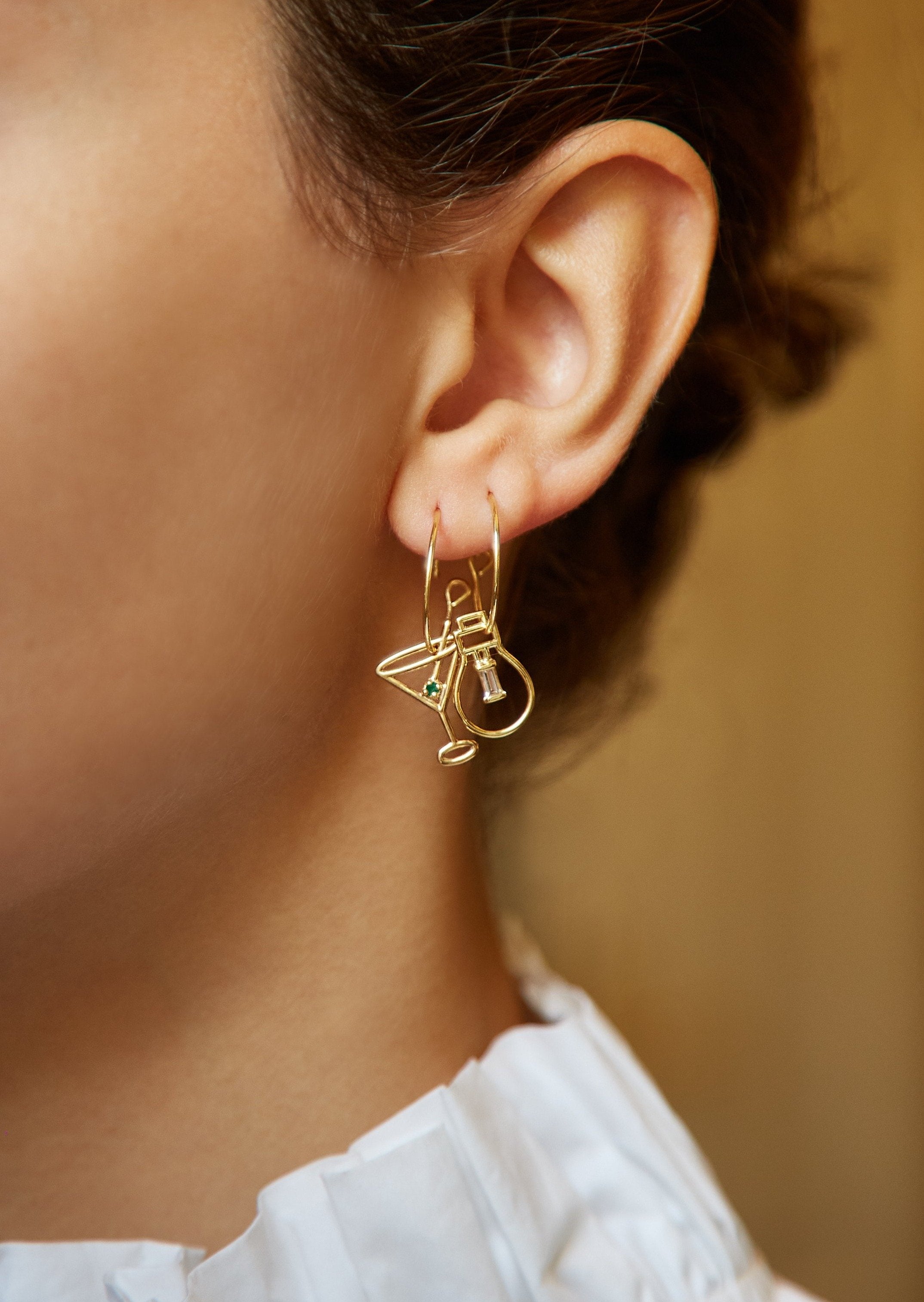 Gold hoop earring with martini drink shaped pendant and small emerald worn by model