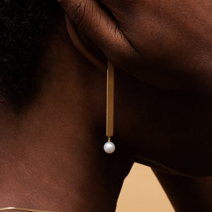 Gold earring with a long bar and a round pearl worn by model