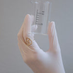 Hand with glove holding a chemistry baker with a house shaped gold ring