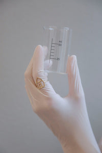 Hand with glove holding a chemistry baker with a house shaped gold ring
