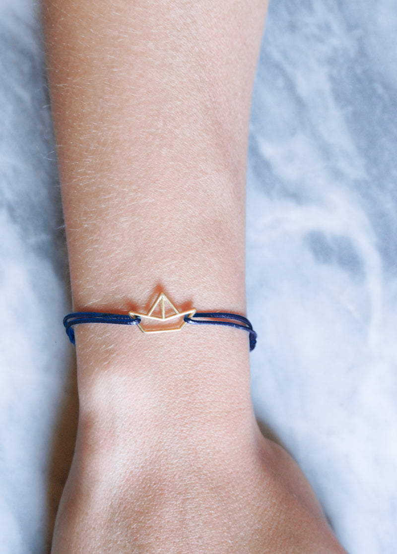 Blue cord bracelet with boat shaped gold pendant on model