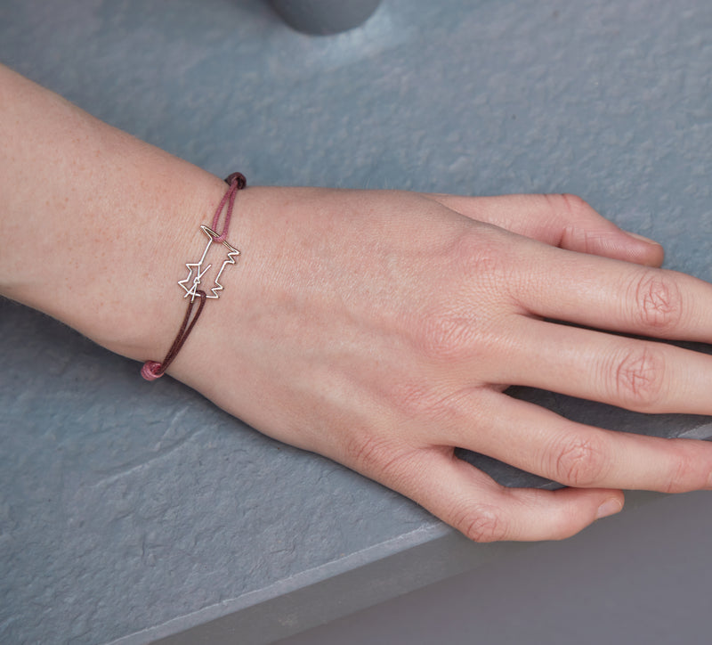 Woman wearing a pink and burgundy cord bracelet with a cat shaped white gold pendant