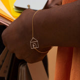 Gold chain bracelet with house shaped pendant and small diamond worn by model