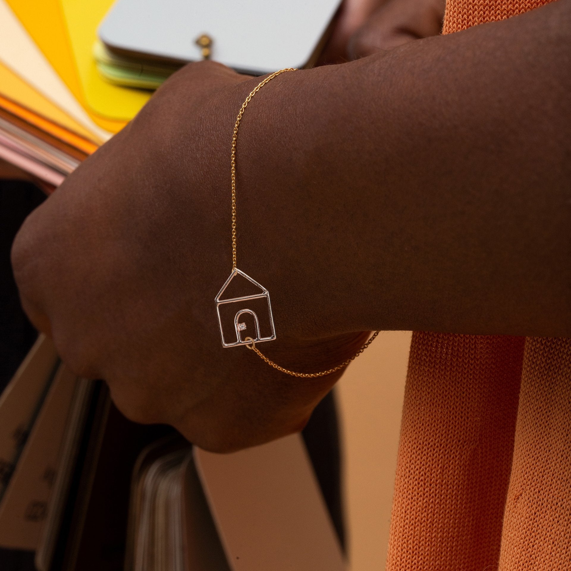 Gold chain bracelet with house shaped pendant and small diamond worn by model