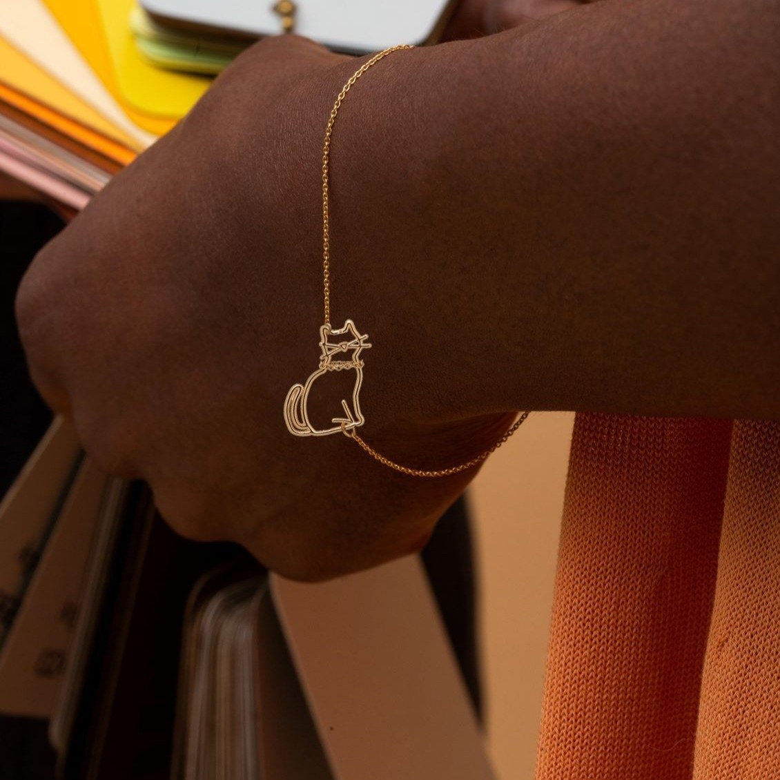 Gold chain bracelet with seated cat shaped pendant worn by model