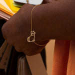 Gold chain bracelet with seated cat shaped pendant worn by model