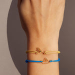 Light yellow eco cord bracelet with a martini drink shaped gold pendant with an small emerald on model's wrist