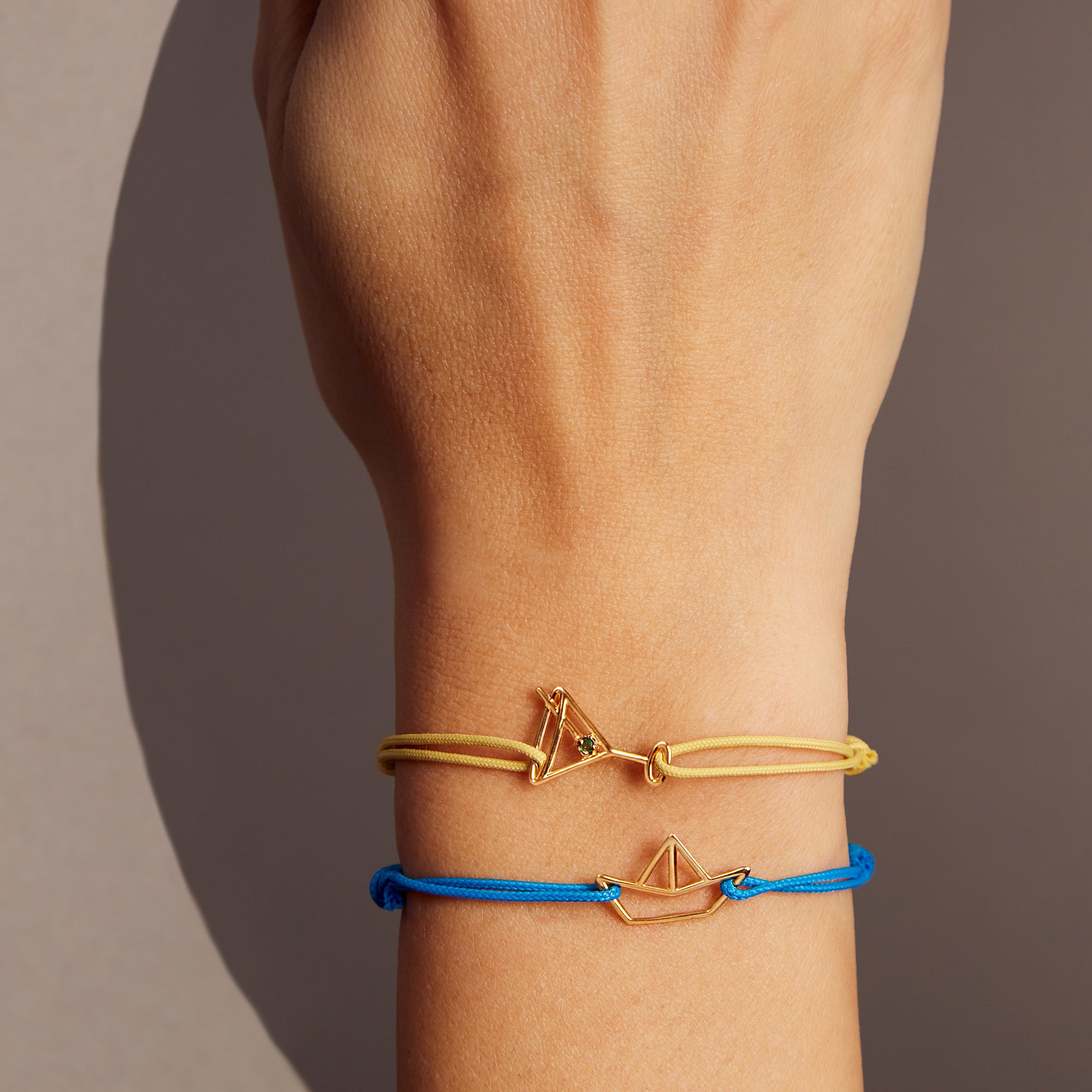Light yellow eco cord bracelet with a martini drink shaped gold pendant with an small emerald on model's wrist