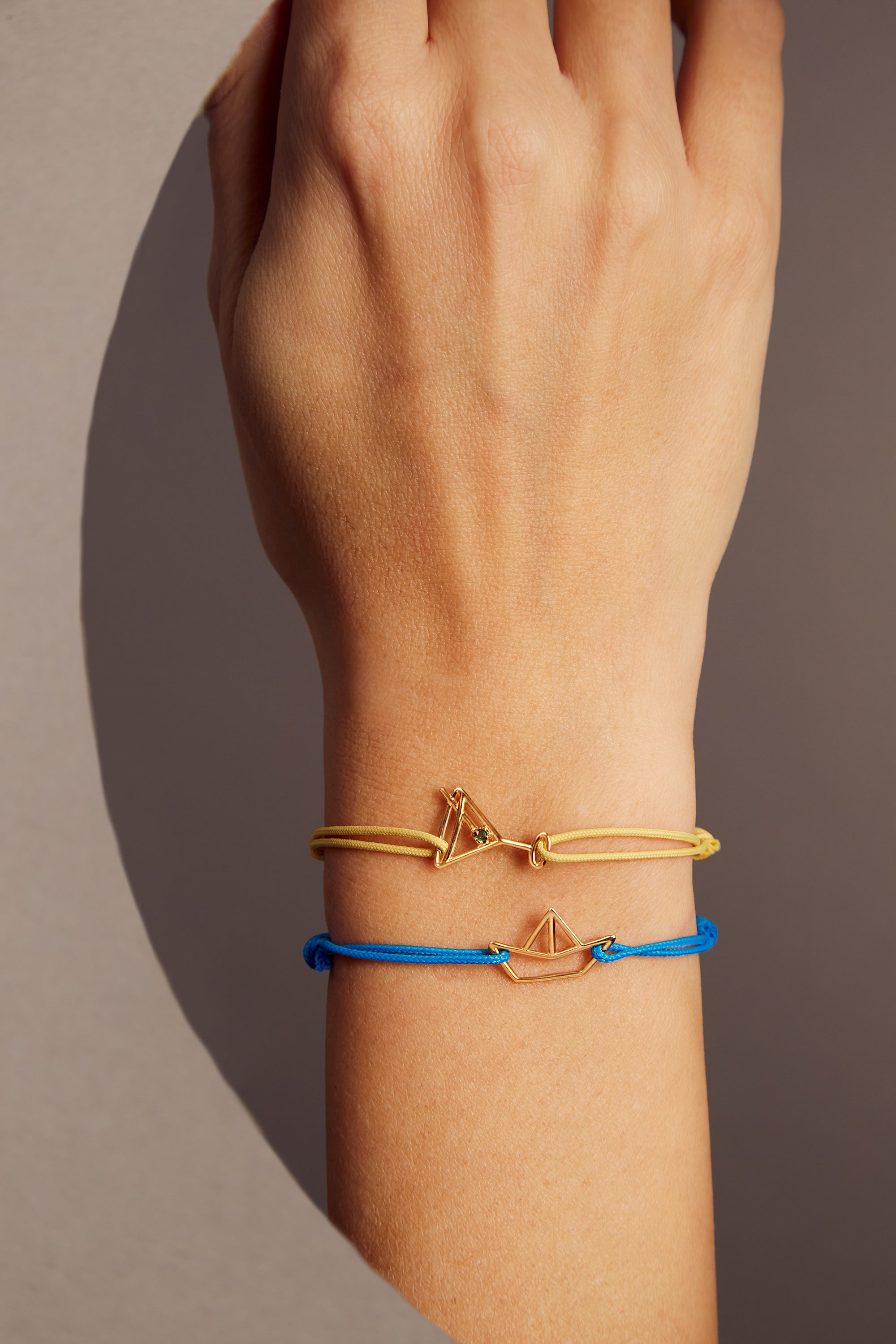 Light yellow eco cord bracelet with a martini drink shaped gold pendant with an small emerald on model's wrist