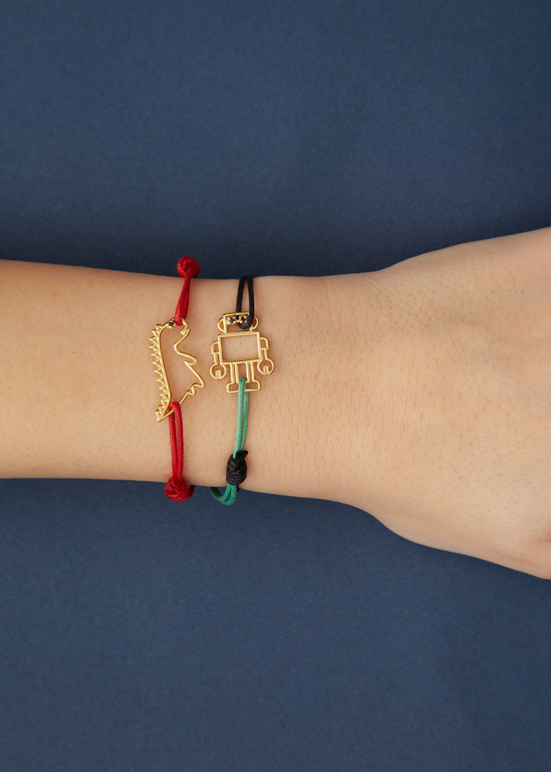 Red cord bracelet with gold dinosaur shaped pendant and small blue sapphire worn by model