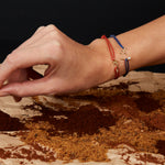 Hand holding carrot earring and wearing bracelets with small gold pendants
