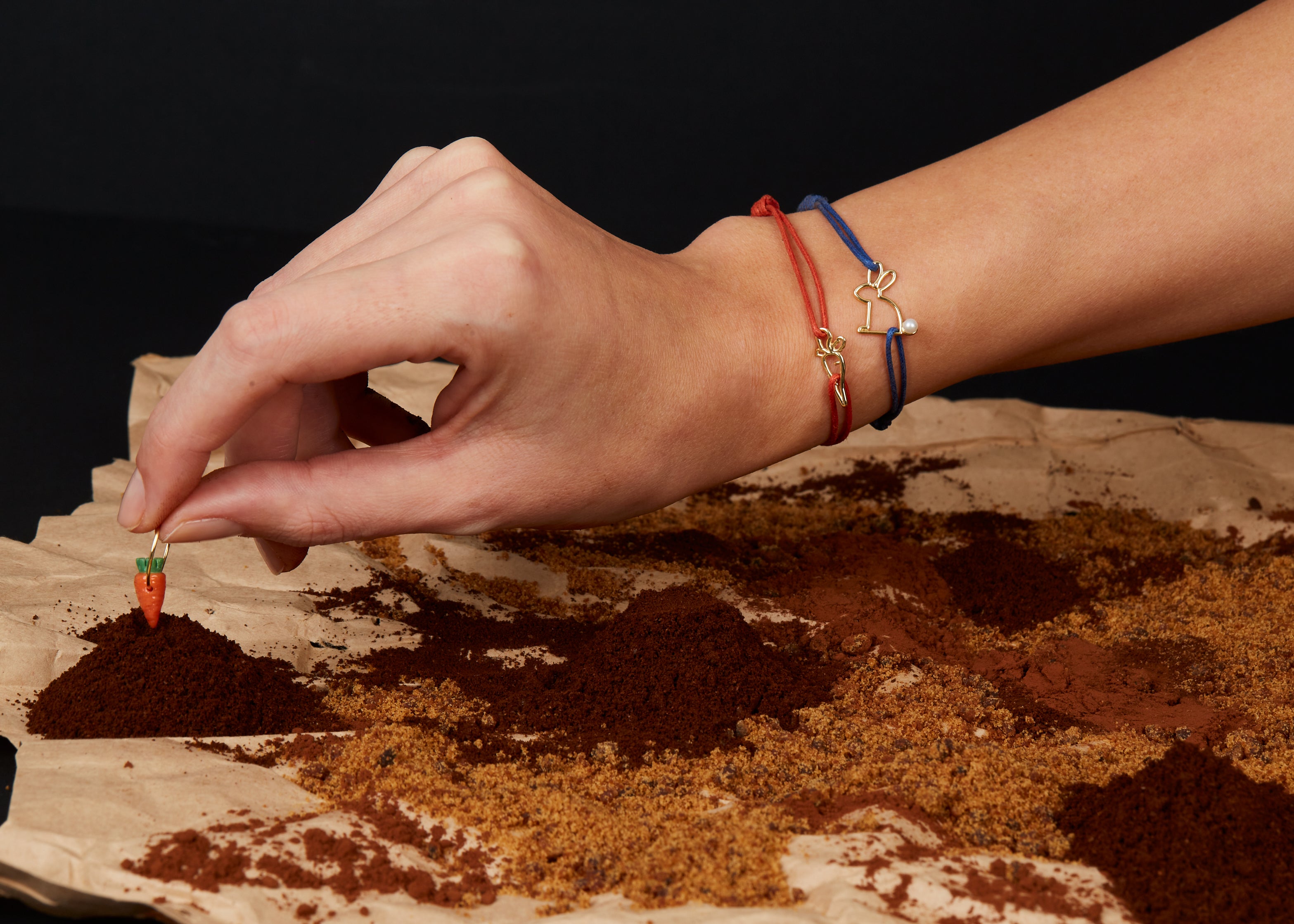 Hand holding carrot earring and wearing bracelets with small gold pendants