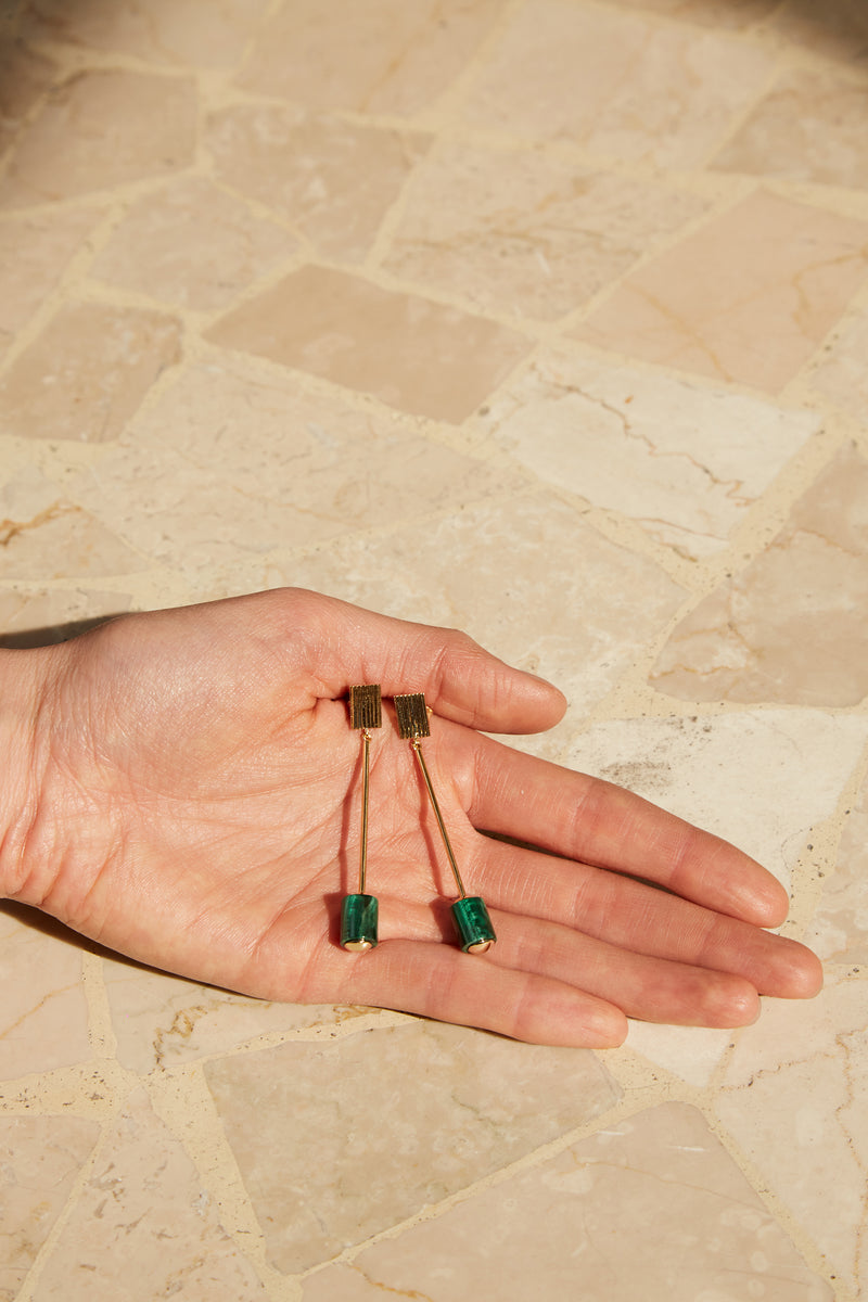 Hands holding long gold earrings with cylinder cut malachite stones