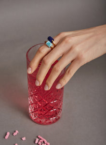 Hand wearing gold rings with amazonite and lapis lazuli stones and pink glass