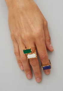 Hand wearing gold square rings with precious stones