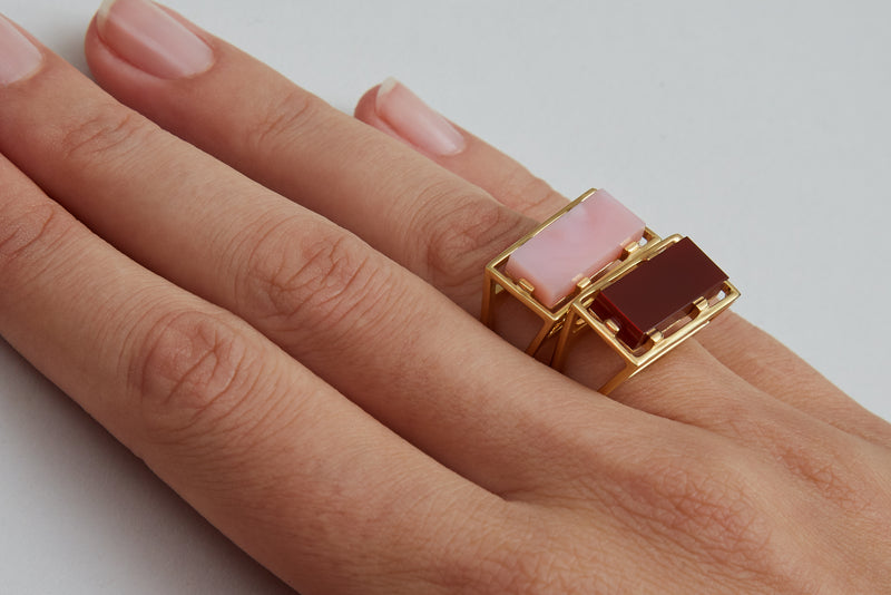 Gold rings with pink opal and carnelian stones on model's hand