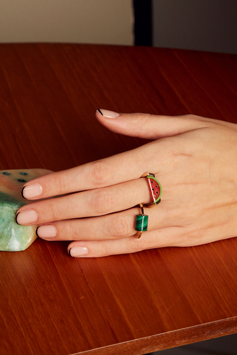 Hand wearing a gold ring with a red coral watermelon slice and a round ring with malachite stone