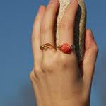 Hand wearing a crocodile shaped gold ring with diamond and a gold ring with a shell in red coral