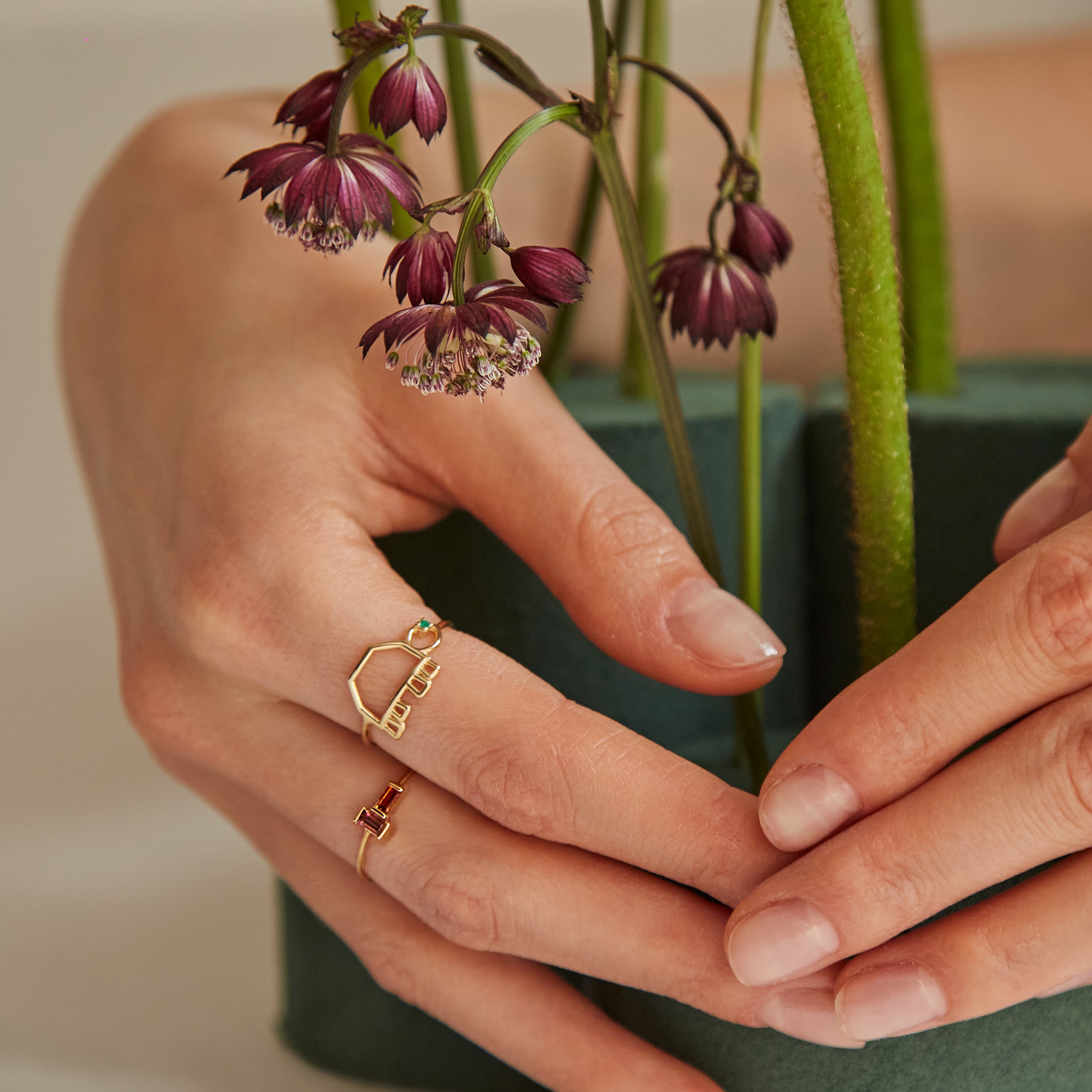Hand with flowers wearing a gold ring shaped like a turtle with a green emerald eye