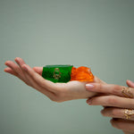 Gold robot shaped ring with blue sapphires as eyes inside a green jelly and model's hands