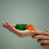 Gold robot shaped ring with blue sapphires as eyes inside a green jelly and model's hands