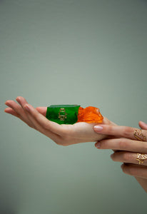 Gold robot shaped ring with blue sapphires as eyes inside a green jelly and model's hands