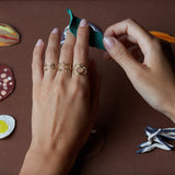 Hands wearing gold rings shaped like shark, cat, camera