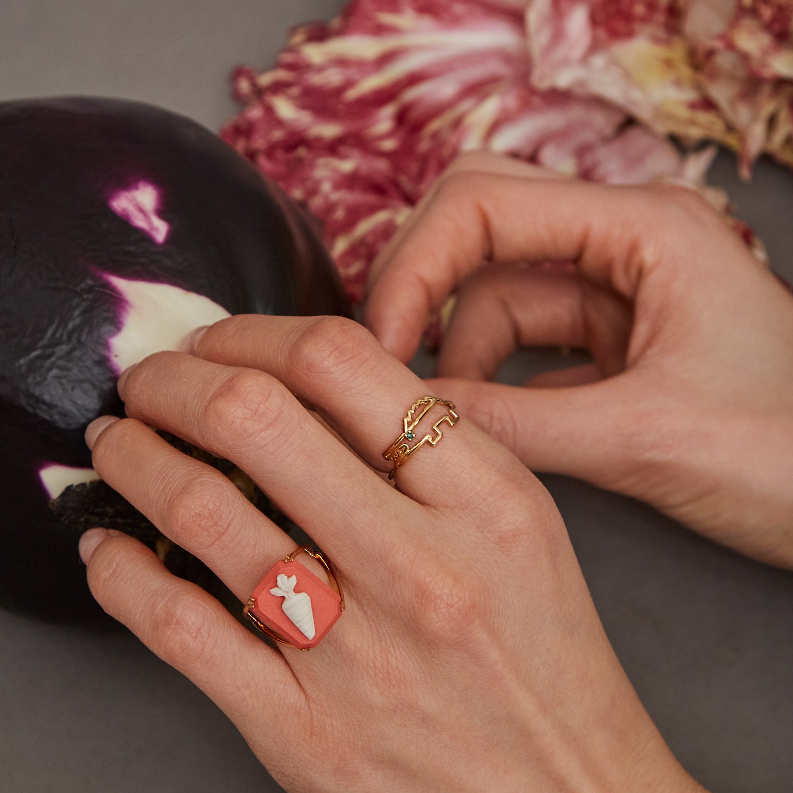 Woman hands holding an eggplant wearing a gold ring with carrot shaped cameo and a crocodile shaped gold ring